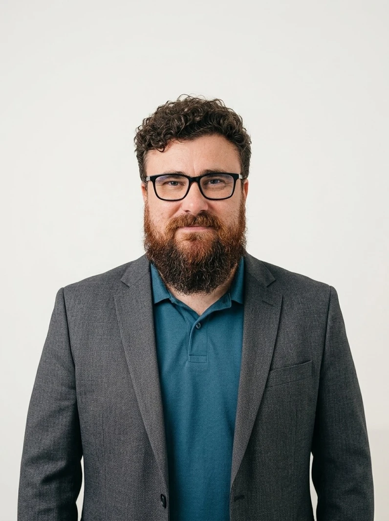Retrato corporativo profissional de Israel Hofman, fundador da Serendip DevOps. Ele possui cabelo cacheado castanho, barba ruiva espessa, óculos de grau pretos e sorri levemente com um olhar confiante. Está trajando um blazer de alfaiataria cinza carvão escuro sobre uma camisa polo azul petróleo. O fundo é off-white com espaço negativo, estilo fotografia de estúdio arquitetônico.
